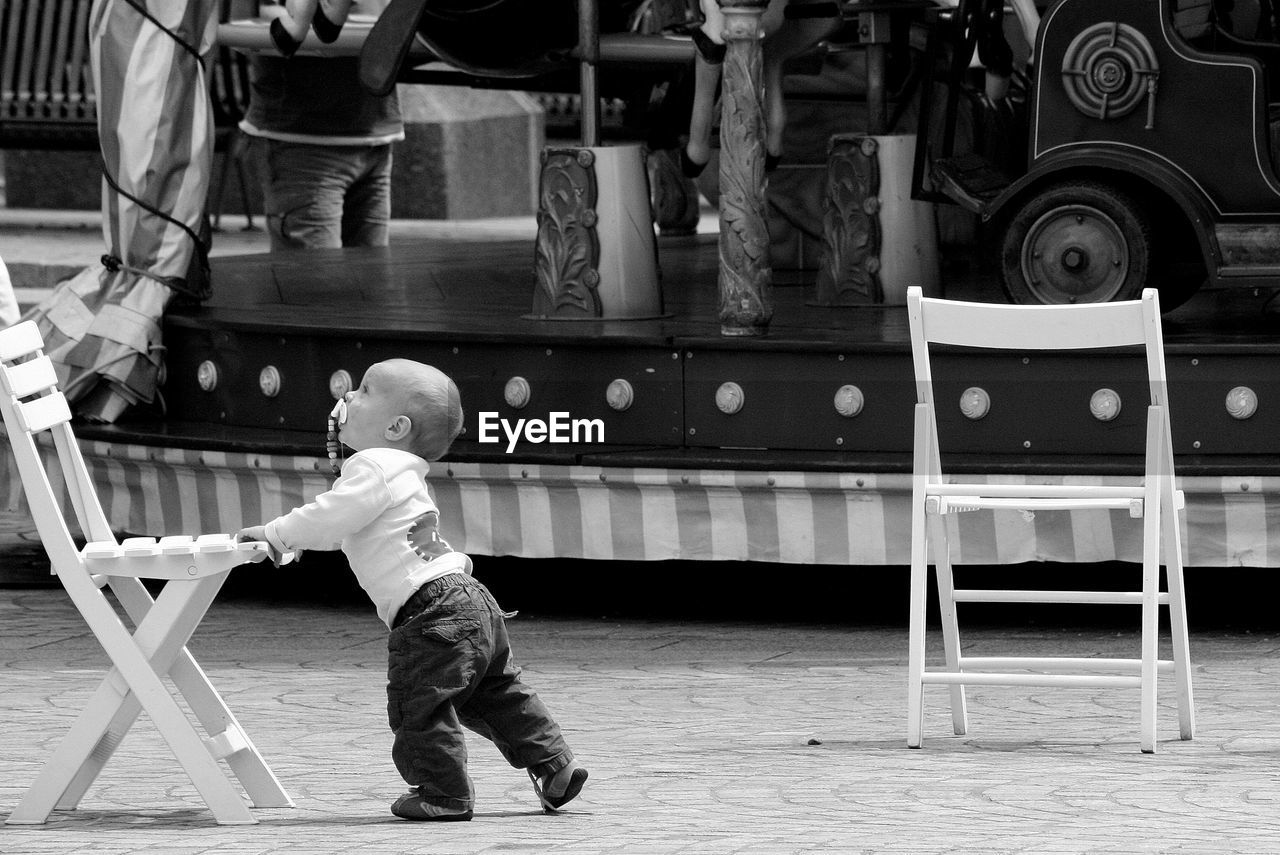 Cute baby boy walking by carousel at amusement park