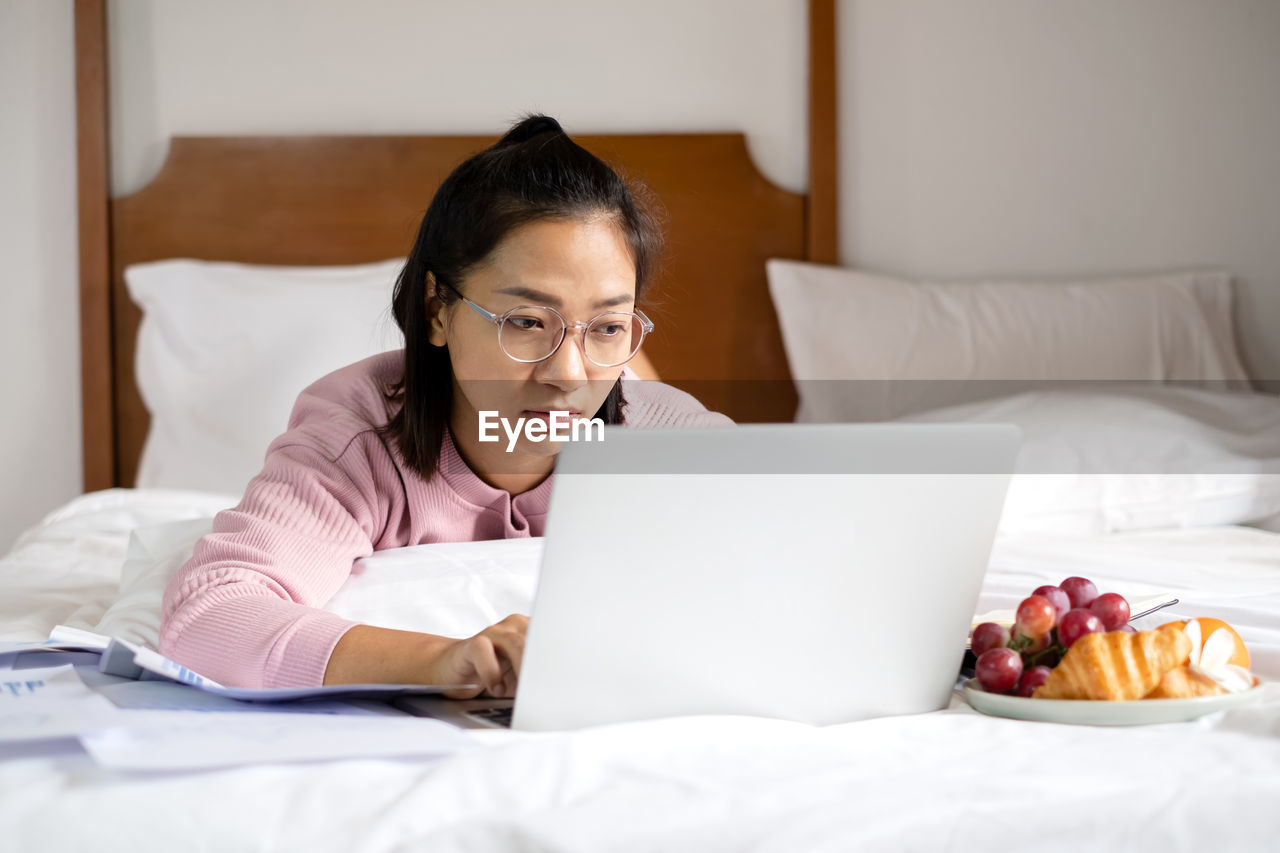 Young businesswoman using laptop while lying on bed