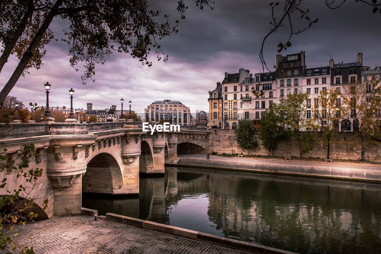 Arch bridge over river by buildings in city against sky