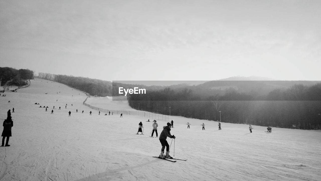 People skiing on snow covered landscape against sky