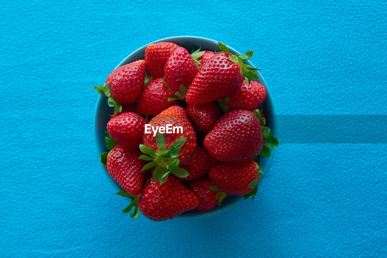 Some delicious strawberries in a bowl with blue background