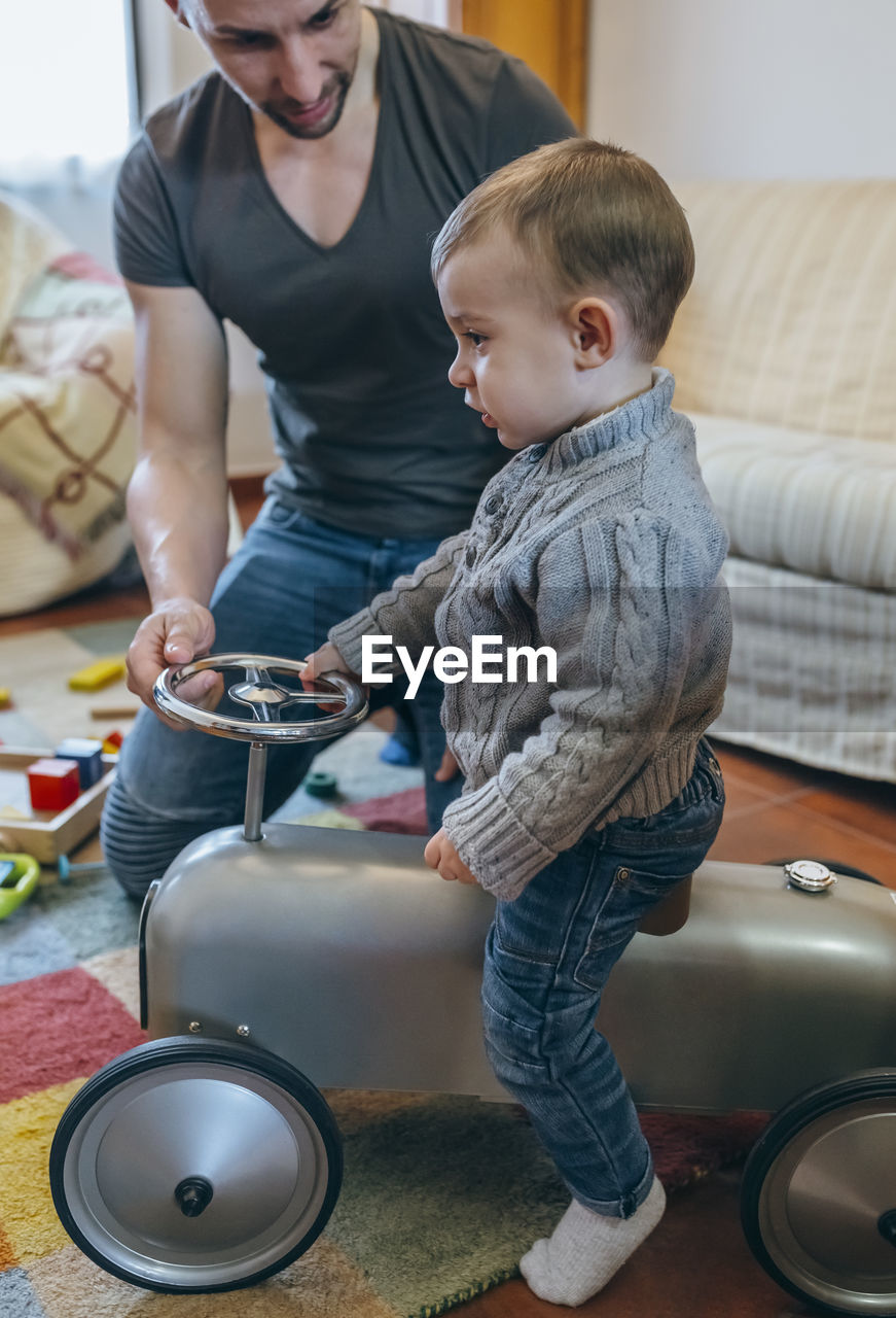 Father playing with son on toy car at home