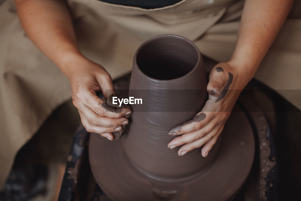 A middle-aged woman works on a potter's wheel, her face is not visible