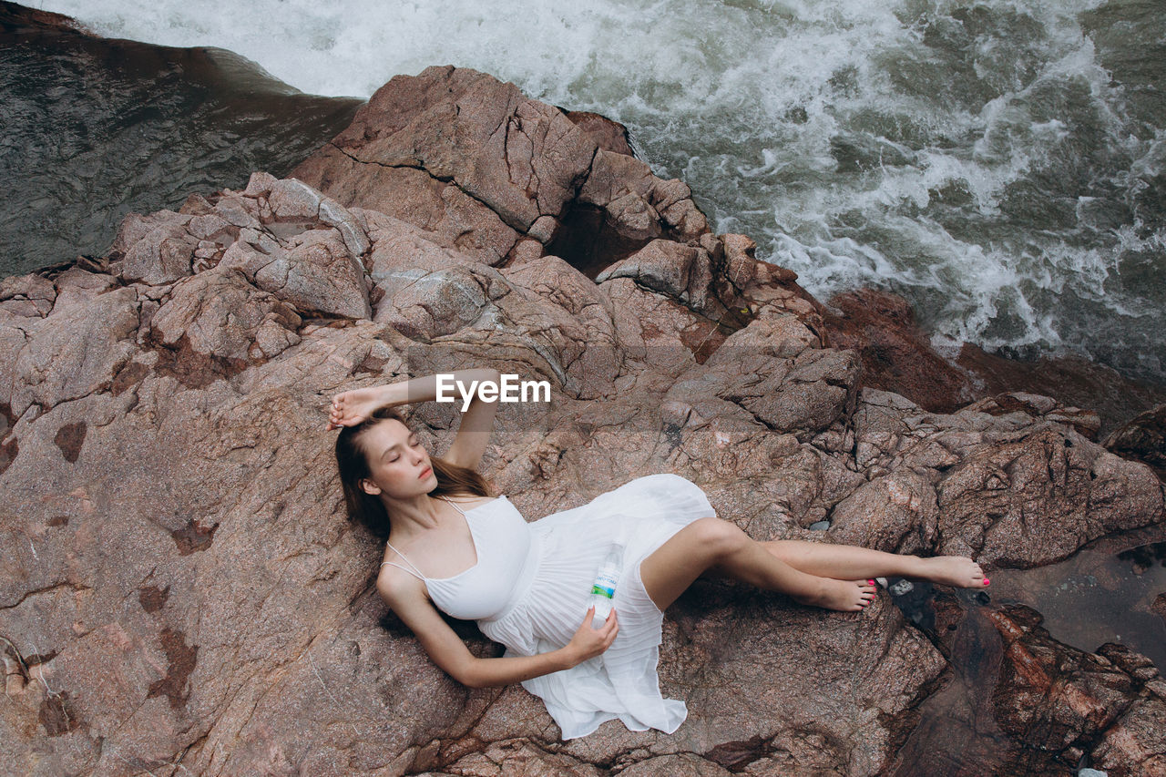 HIGH ANGLE VIEW OF WOMAN RELAXING ON ROCK