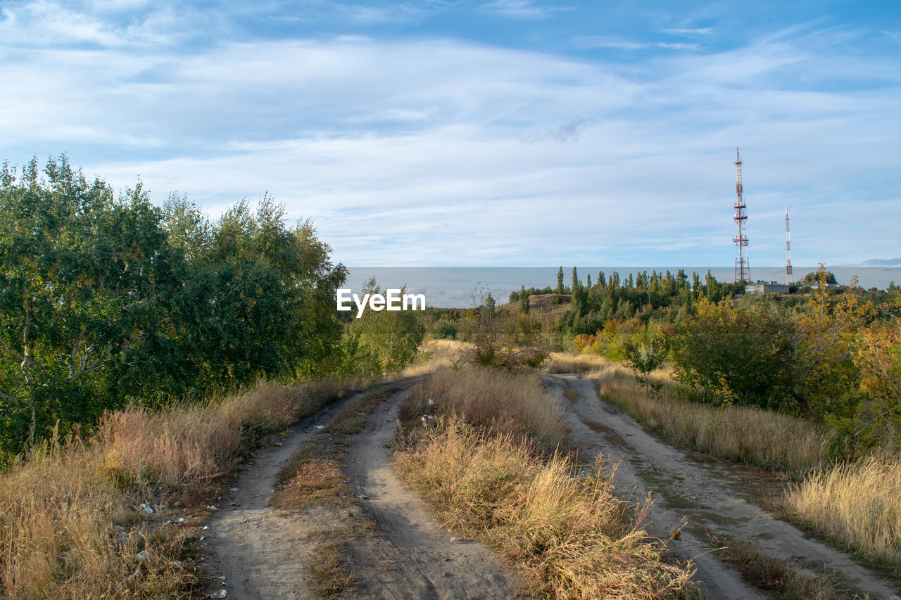 DIRT ROAD PASSING THROUGH LANDSCAPE AGAINST SKY