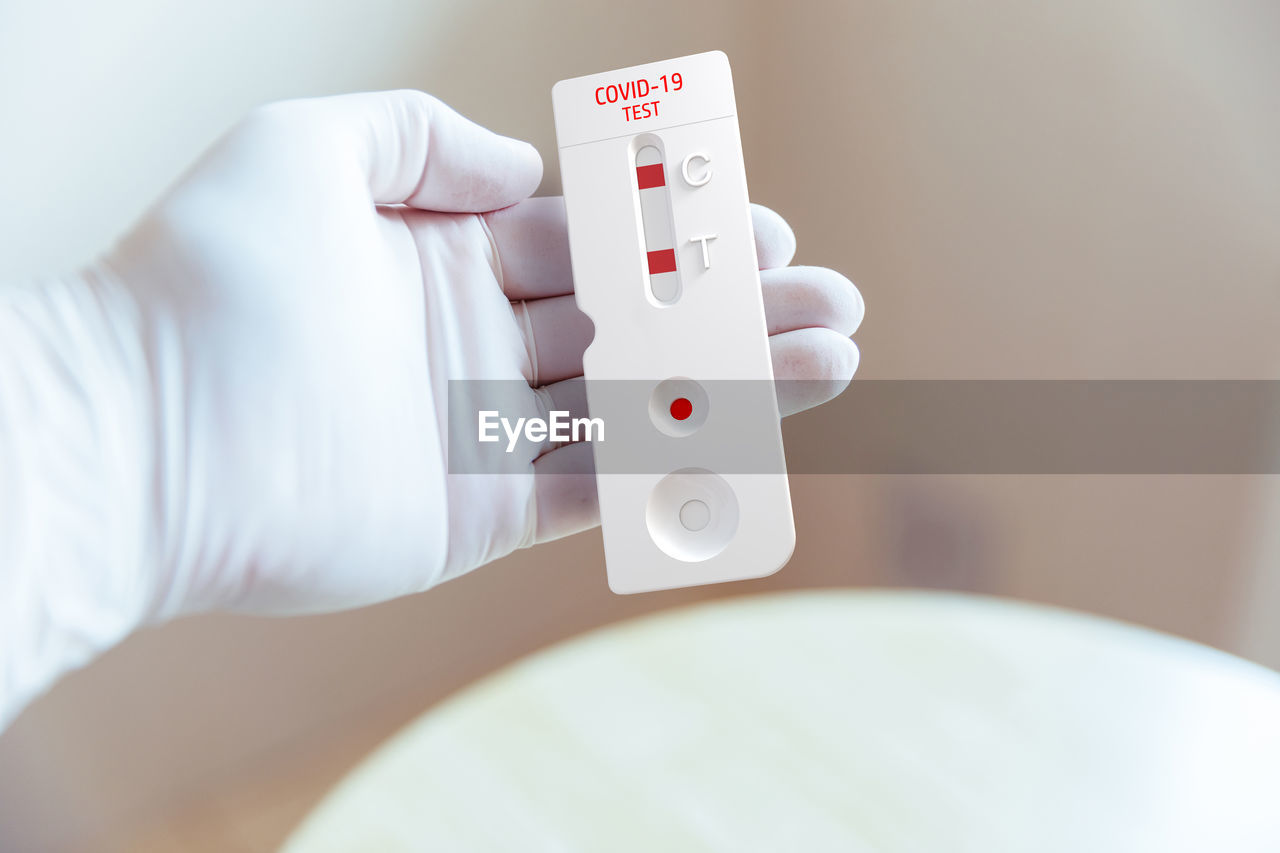 Gloved doctor's hand holding the rapid test result against the covid-19. positive result.