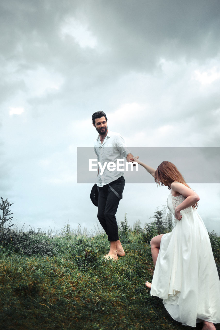 Man holding hands of woman while walking on grassy field