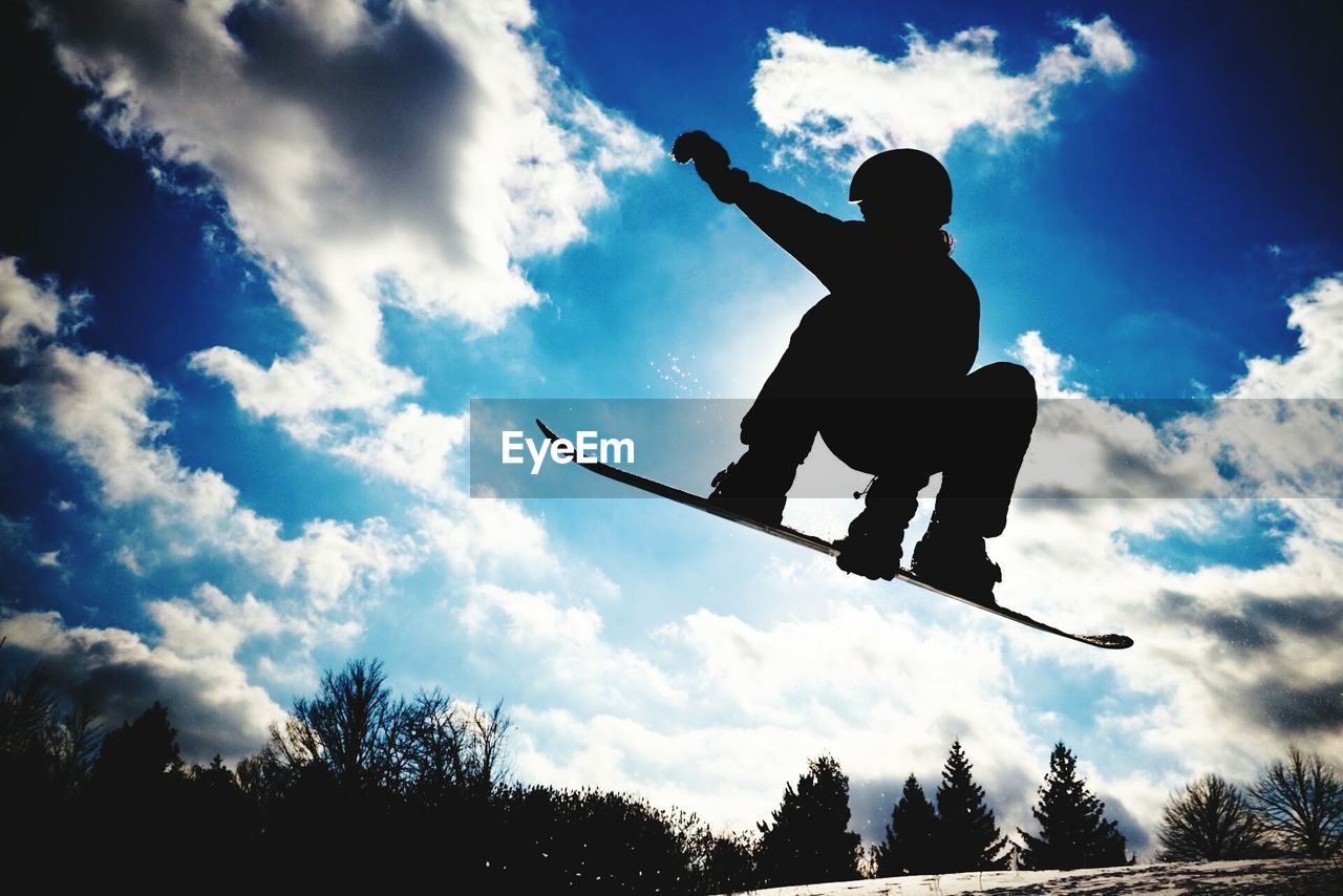 Silhouette person snowboarding mid-air against sky