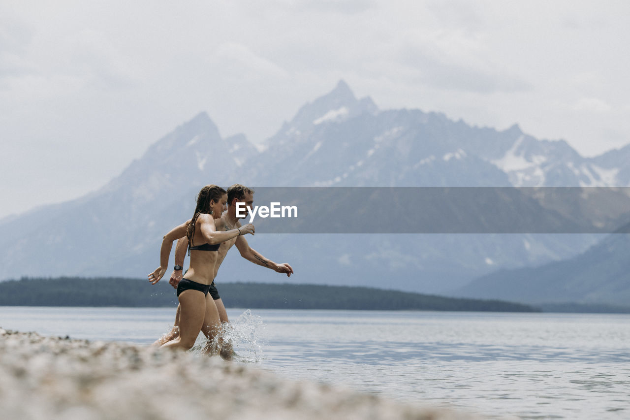 Couple runs into jackson lake for a swim, tetons in the background