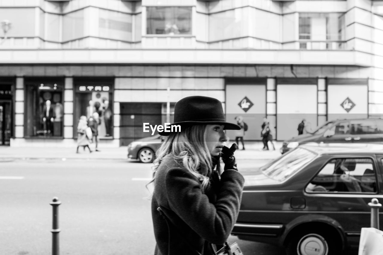 REAR VIEW OF WOMAN STANDING ON STREET AGAINST ROAD