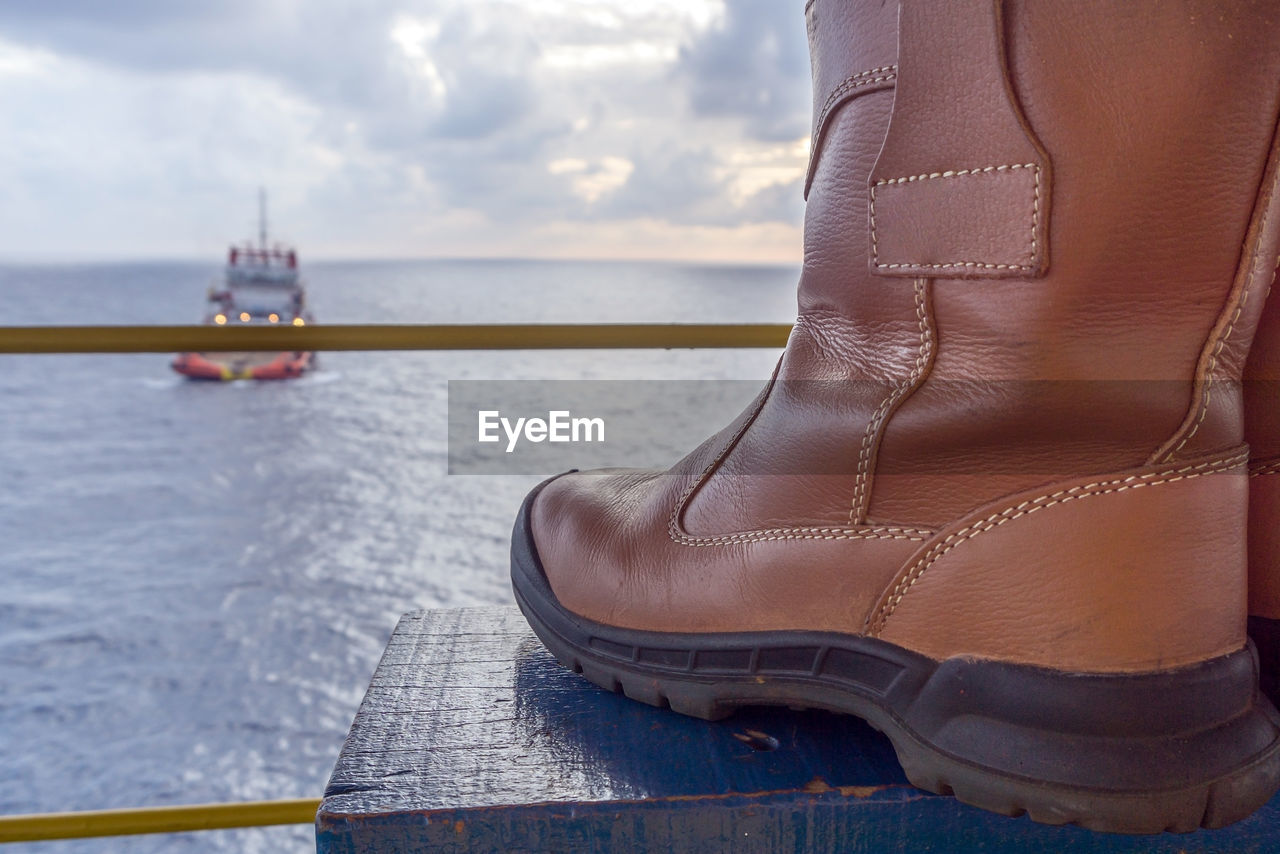 Close-up of boots at beach against sky