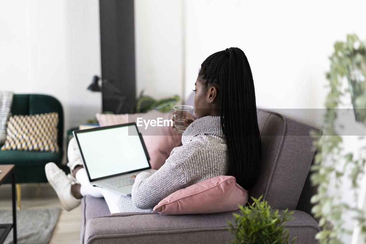 Young businesswoman drinking water working on laptop sitting at home