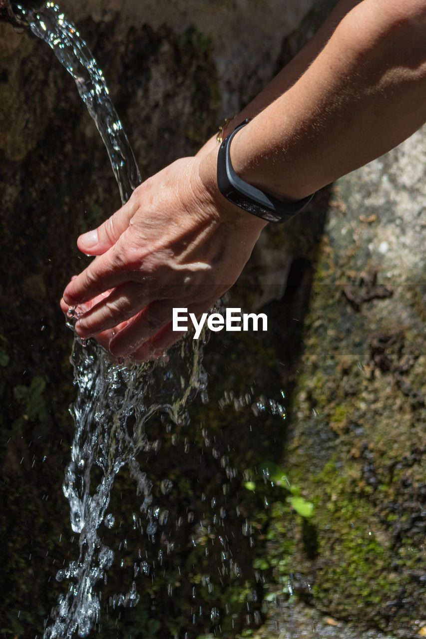 Cropped image of hand by splashing water fountain outdoors