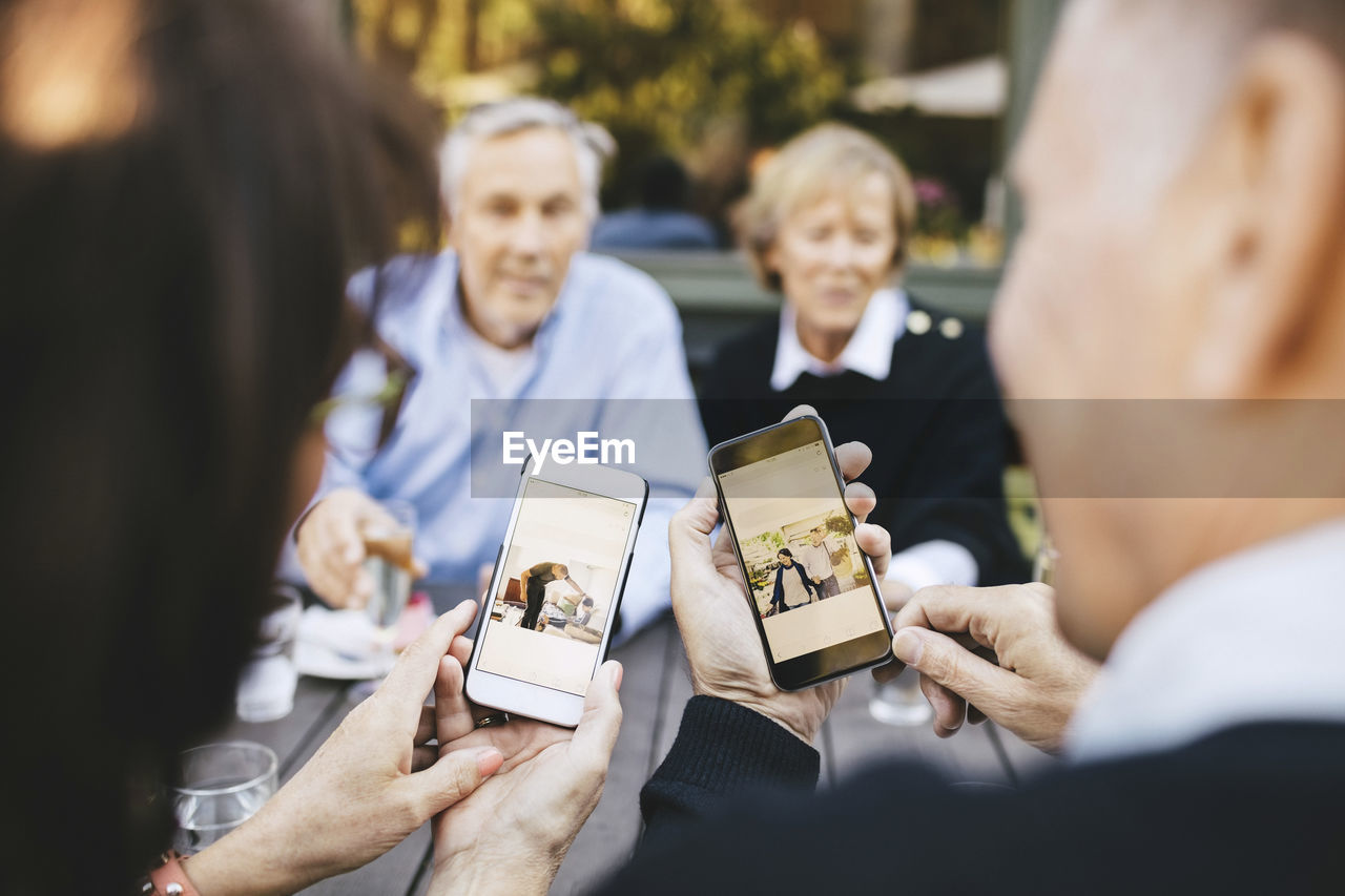 Senior couple looking at photos on mobile phones at outdoor restaurant