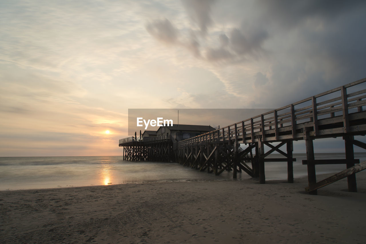 Pier on beach against sky during sunset