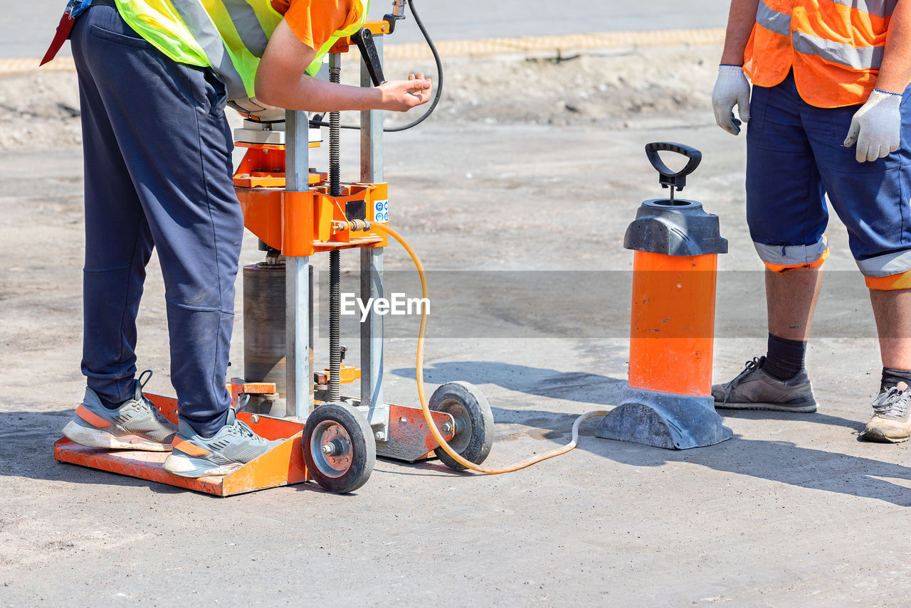 Road builders set up a gasoline drilling machine to cut asphalt concrete samples on a sunny day.