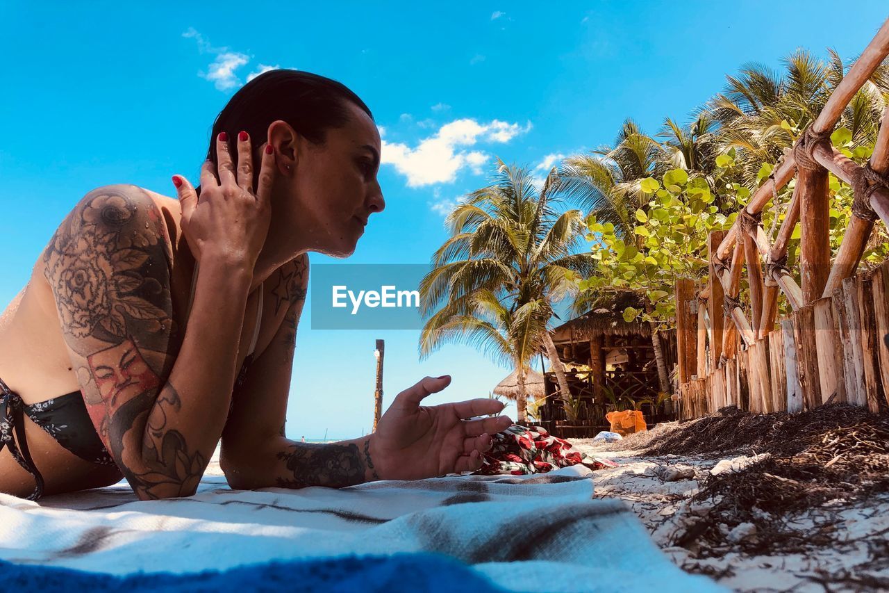 Woman with tattoo lying at beach against blue sky