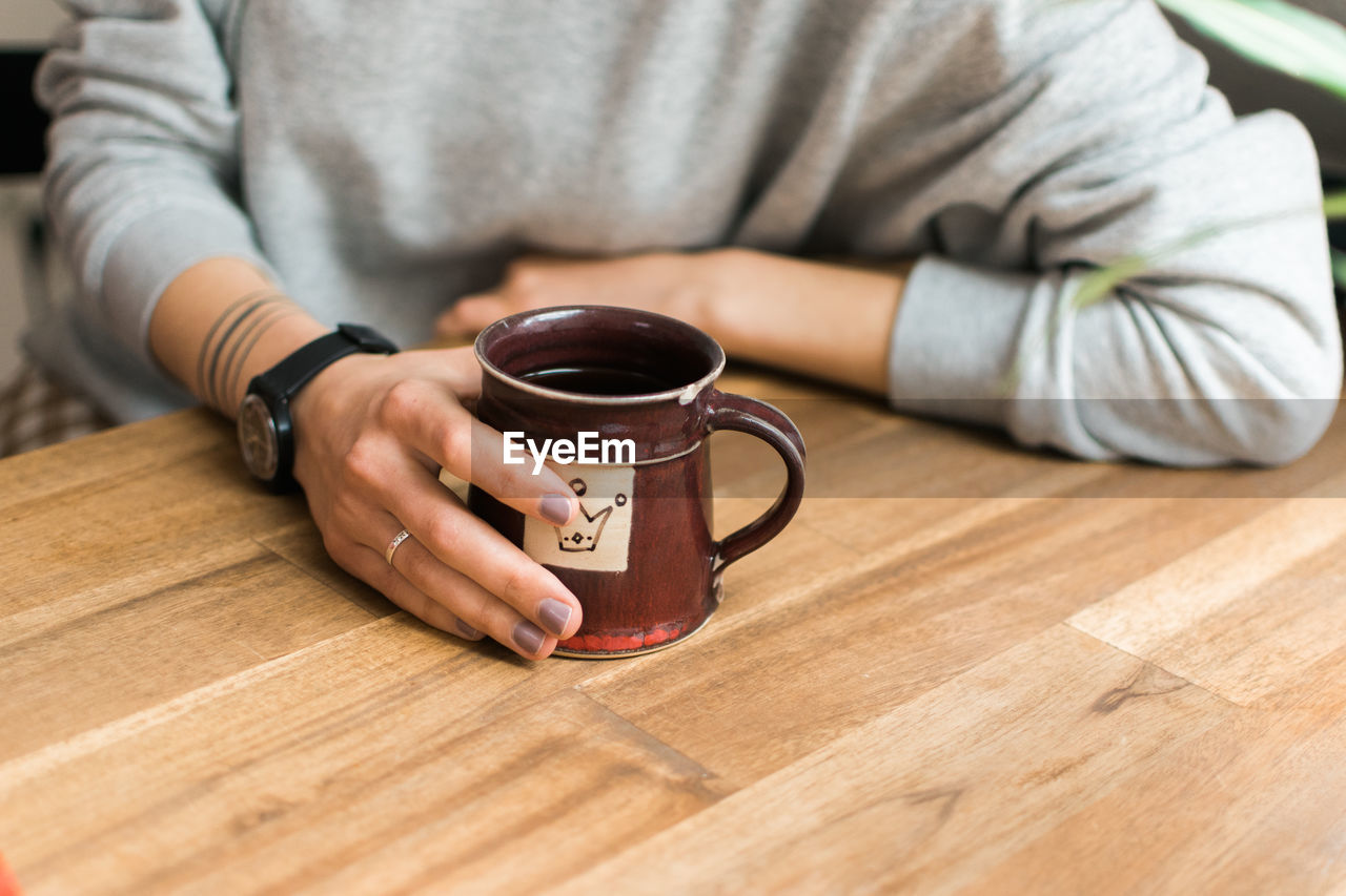 Midsection of woman holding coffee cup on table at home