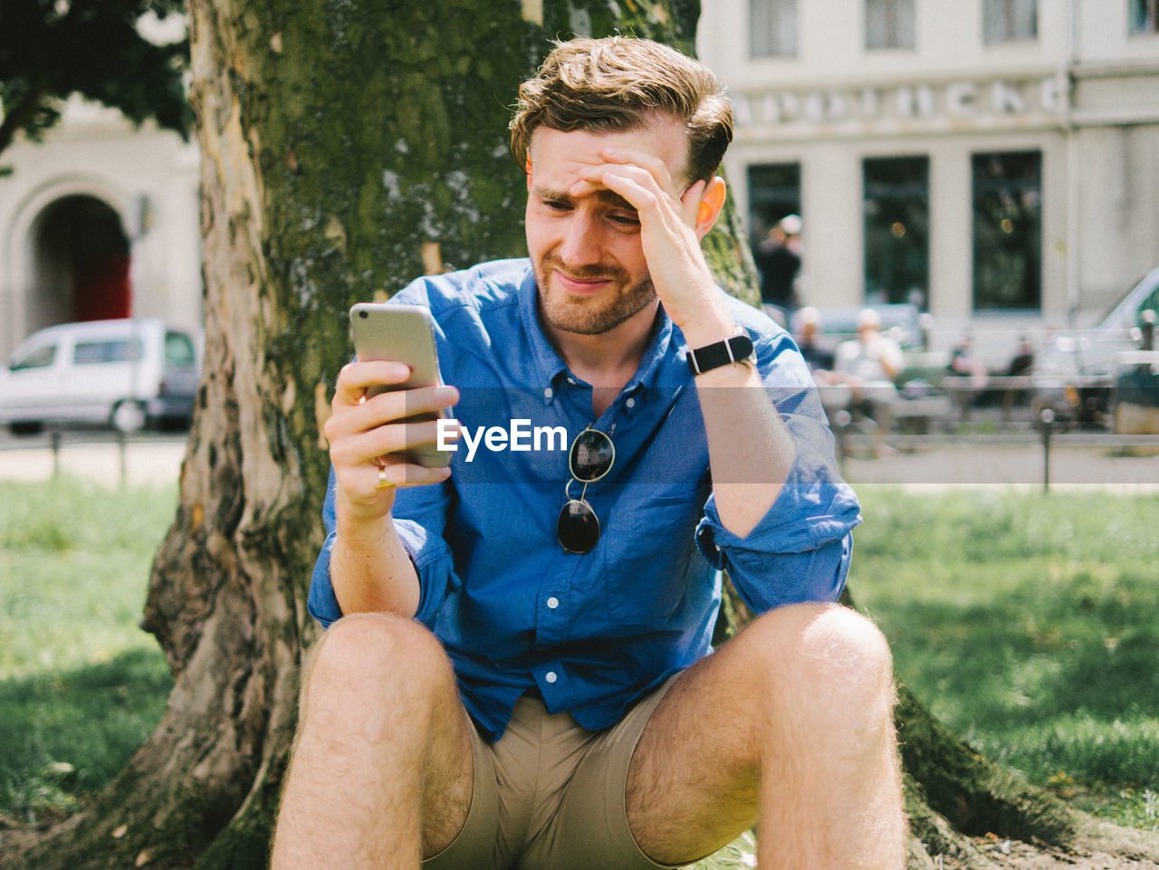 Disappointed man using mobile phone while sitting by tree