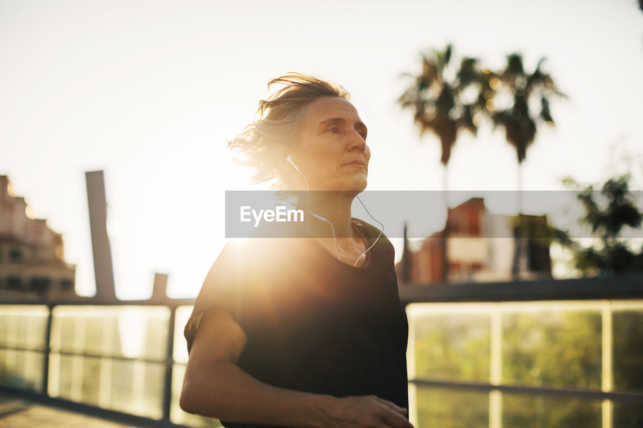 Thoughtful woman looking away while listening music at bridge during sunset