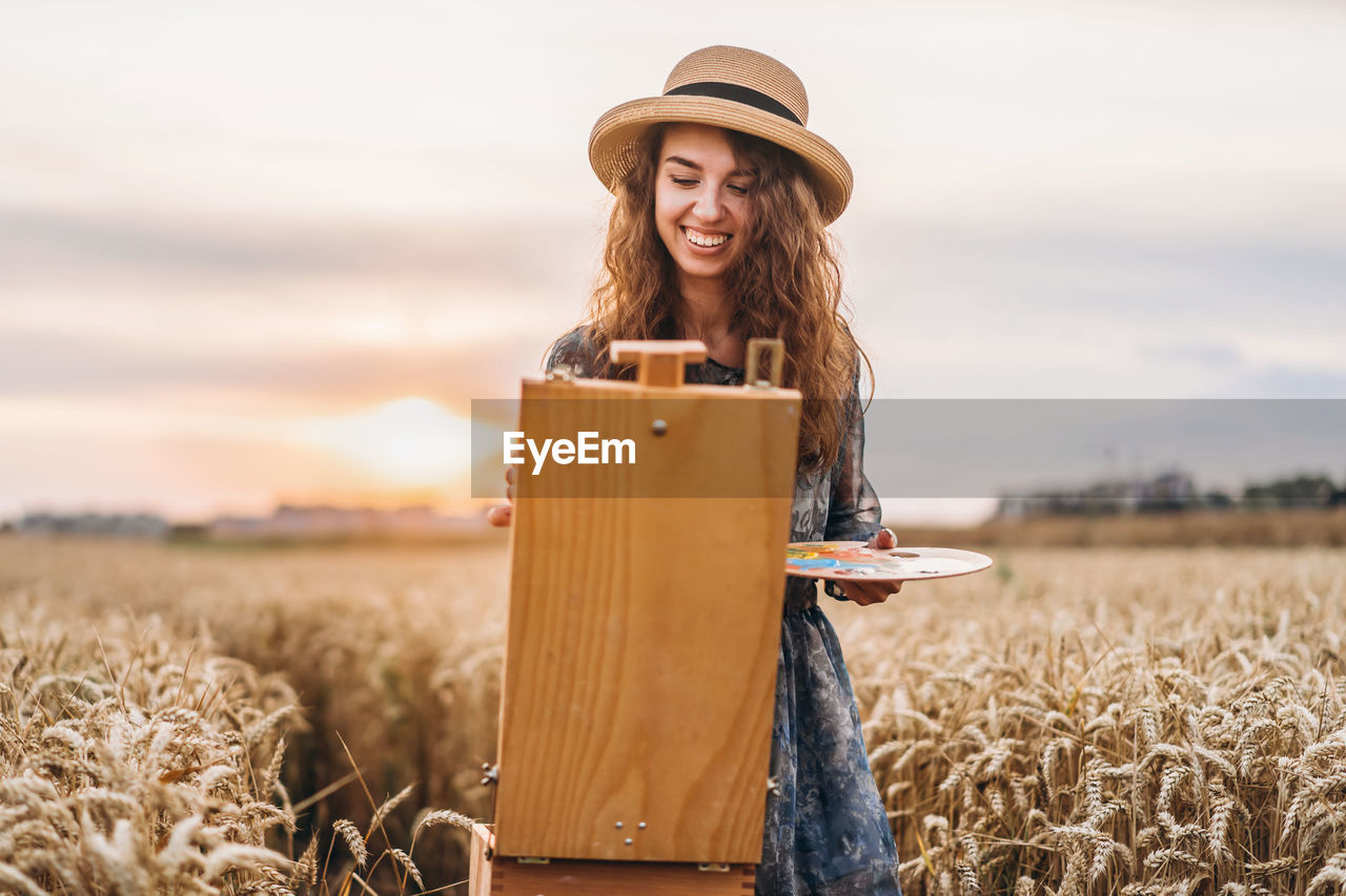 Smiling young woman painting on easel