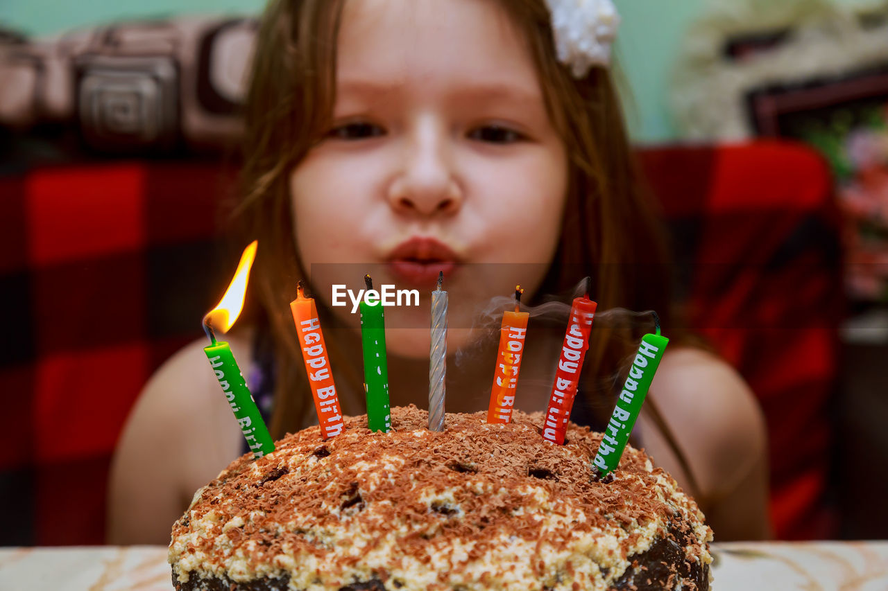 Close-up portrait of smiling girl sitting by cake at home