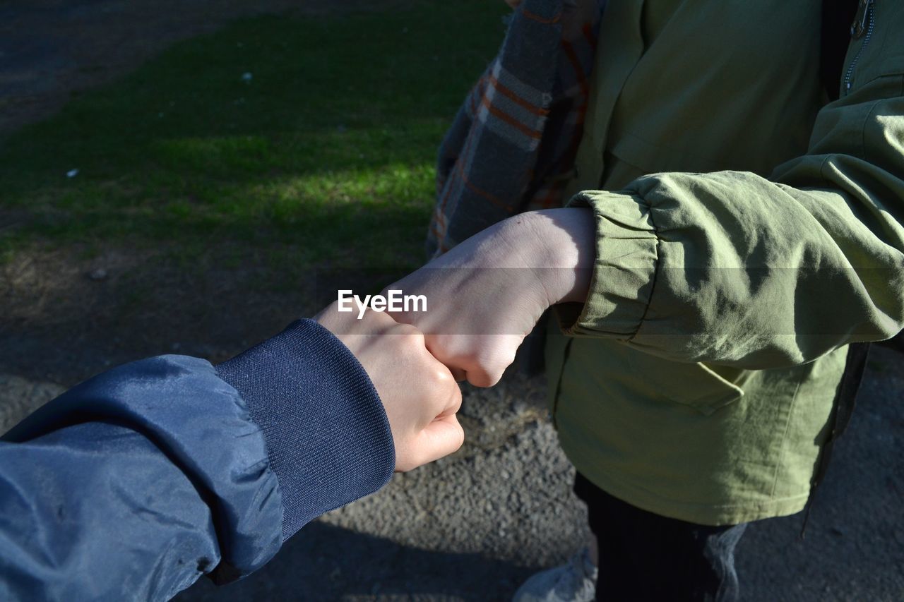 Midsection of friends fist bumping on footpath during sunny day