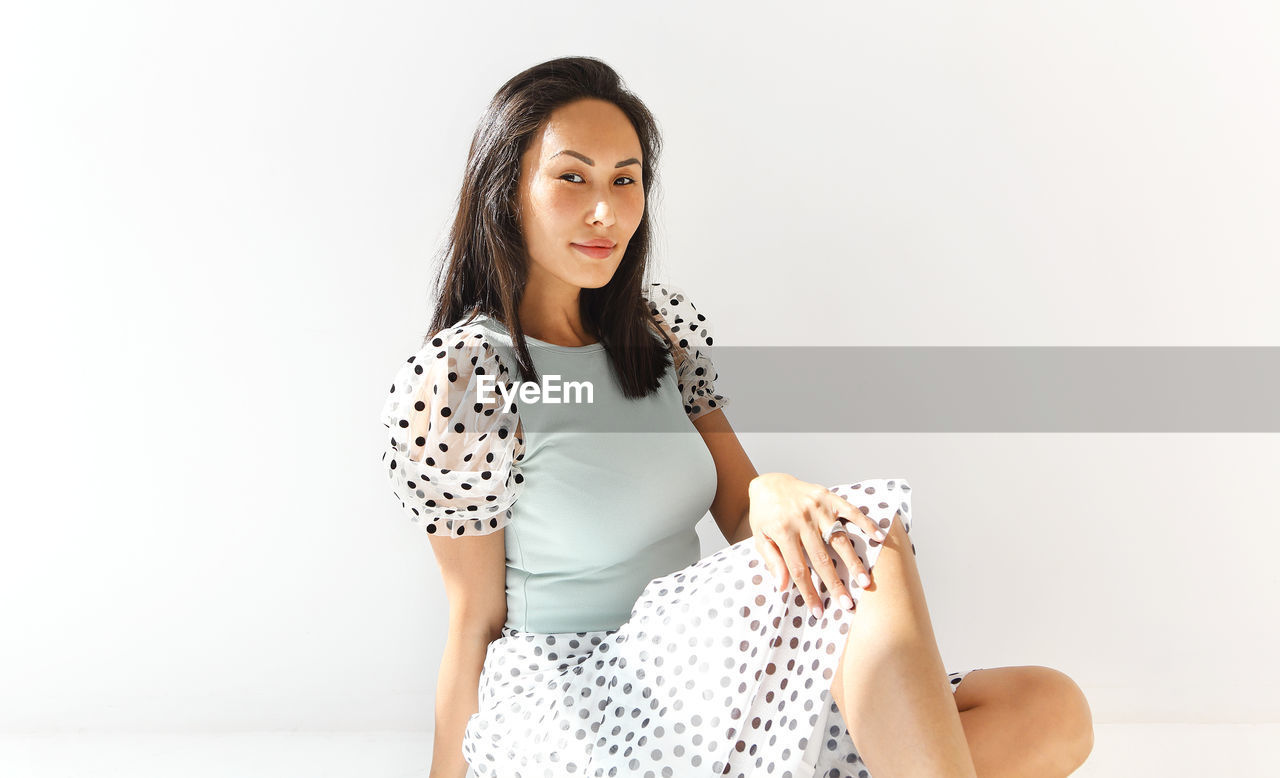 BEAUTIFUL YOUNG WOMAN SITTING AGAINST GRAY BACKGROUND