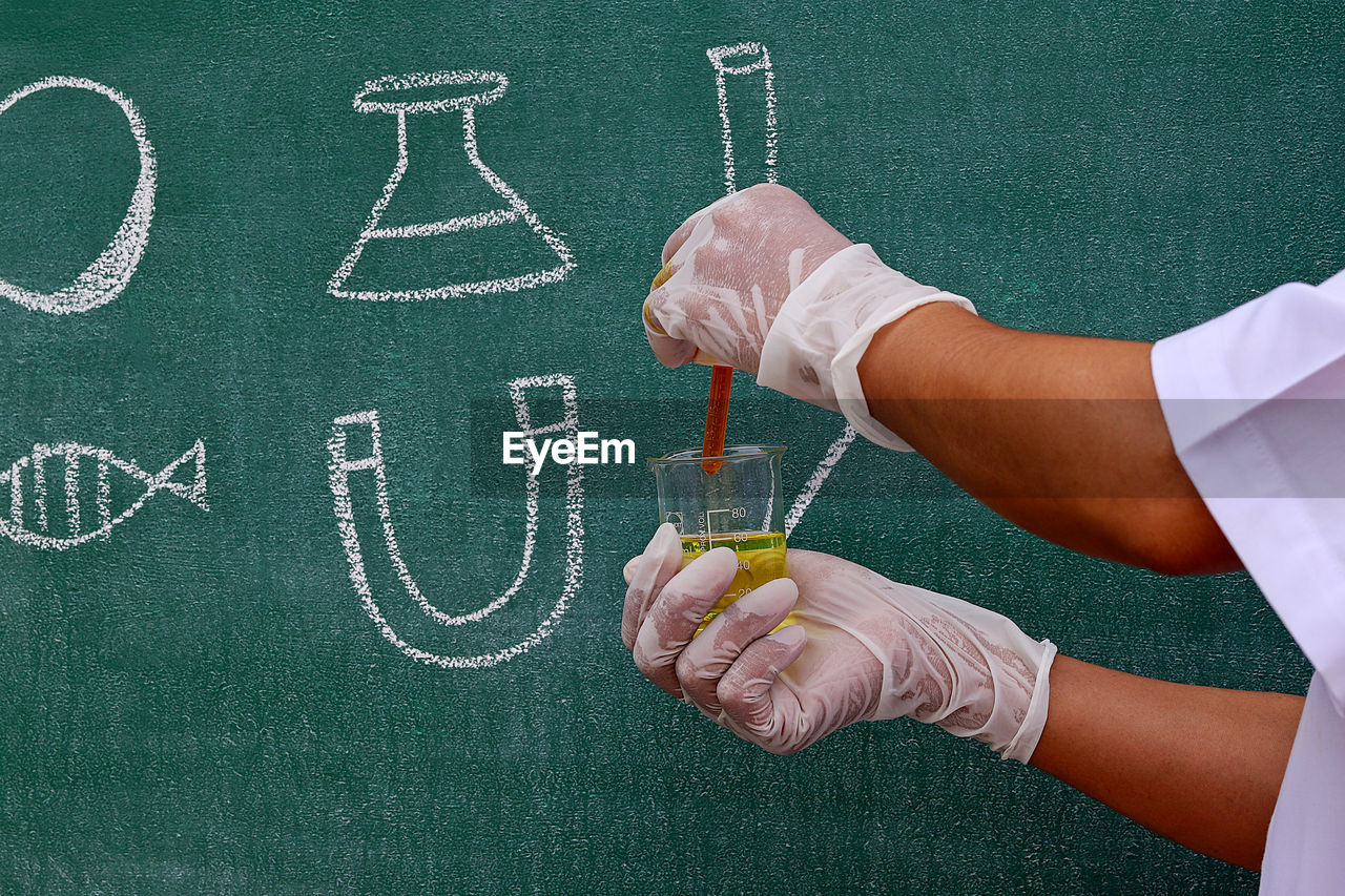 Cropped hands of scientist examining laboratory equipment by blackboard