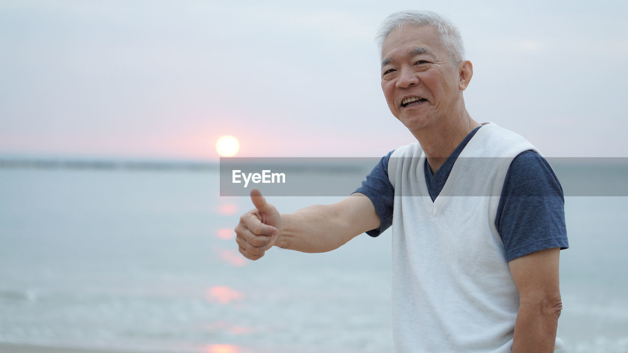 Man gesturing against sea during sunset