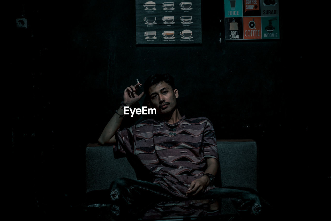 YOUNG MAN LOOKING AWAY WHILE SITTING ON SEAT IN FRONT OF ROOM