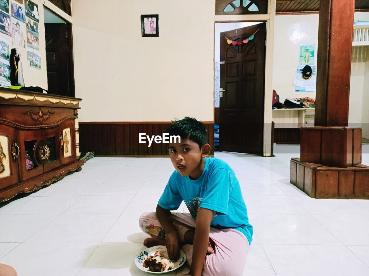 Portrait of boy eating food while sitting on floor at home