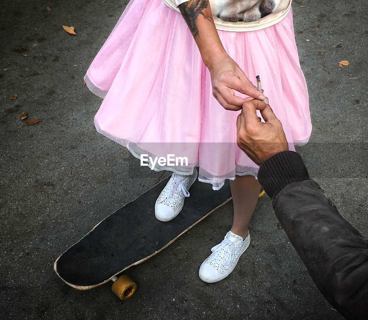 Low section of woman on skateboard taking joint from man