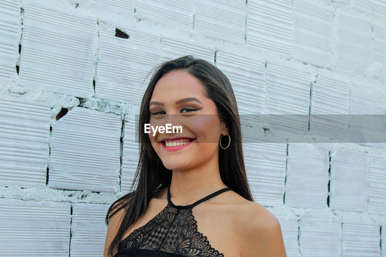 PORTRAIT OF YOUNG WOMAN SMILING AGAINST WALL