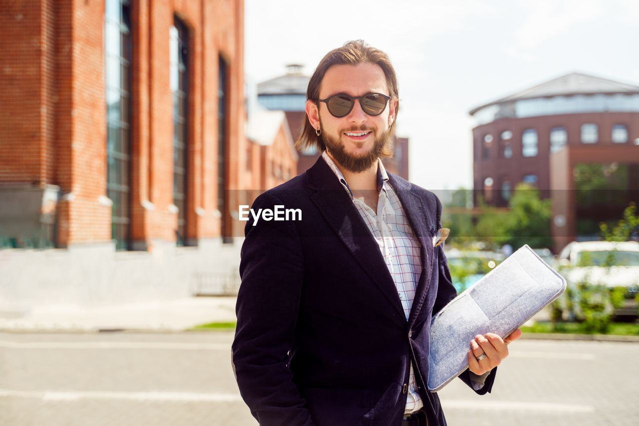 Portrait of smiling businessman holding document standing outdoors