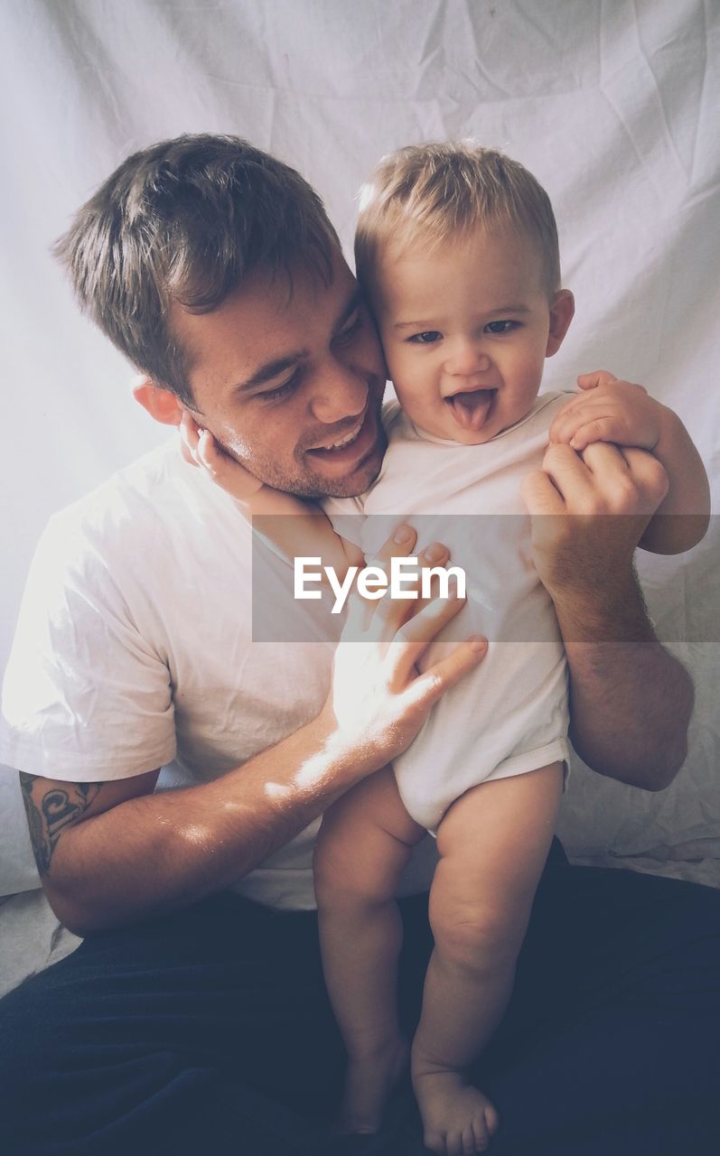 Smiling man holding his son while sitting on bed