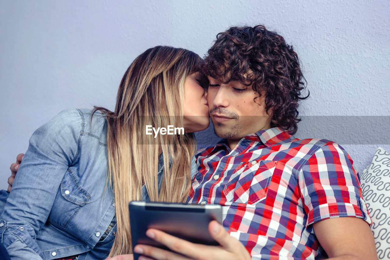 Close-up of woman kissing boyfriend while using digital tablet at home