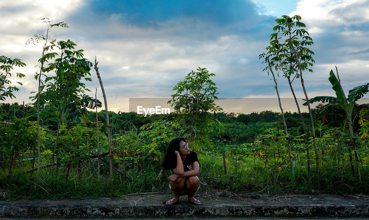 Full length of woman crouching on field against sky