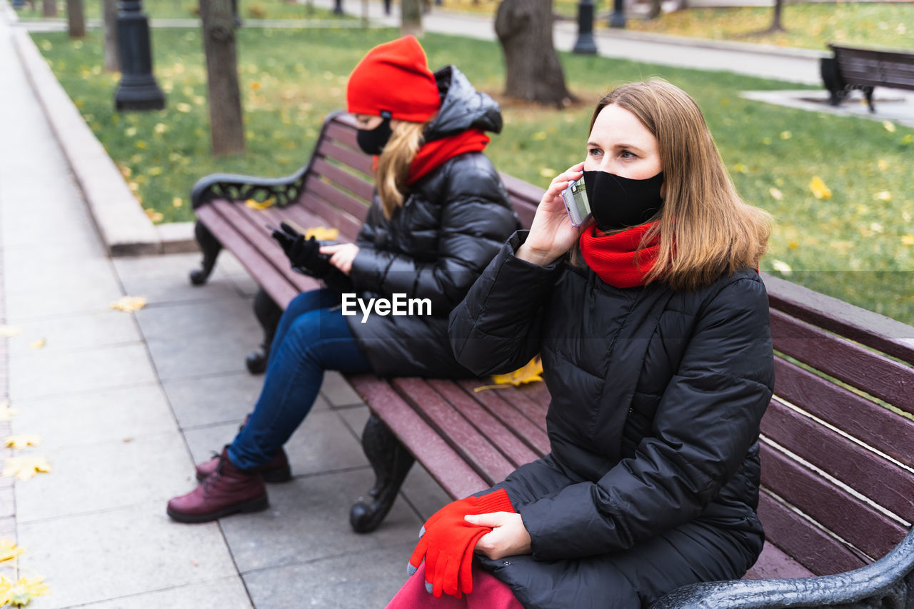 WOMEN SITTING ON BENCH WITH MOBILE PHONE