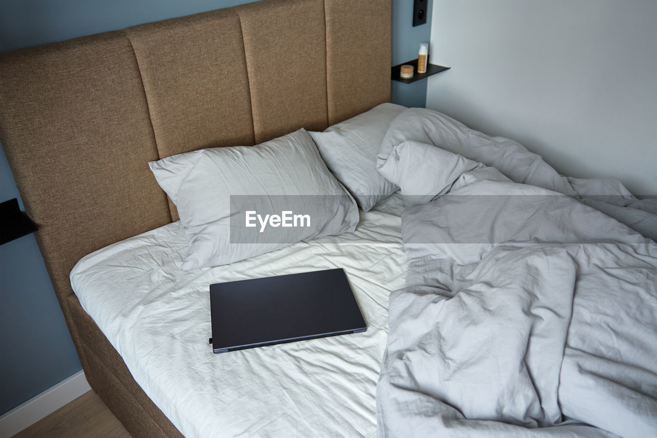 Unmade bed with pillows and crumpled bedsheets and open laptop