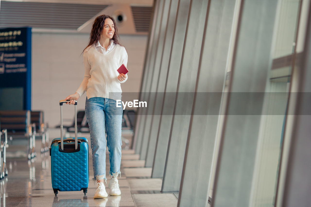 Full length of woman with luggage walking at airport