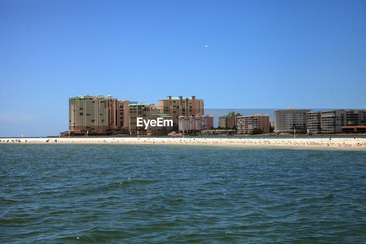 Sea by buildings against clear blue sky