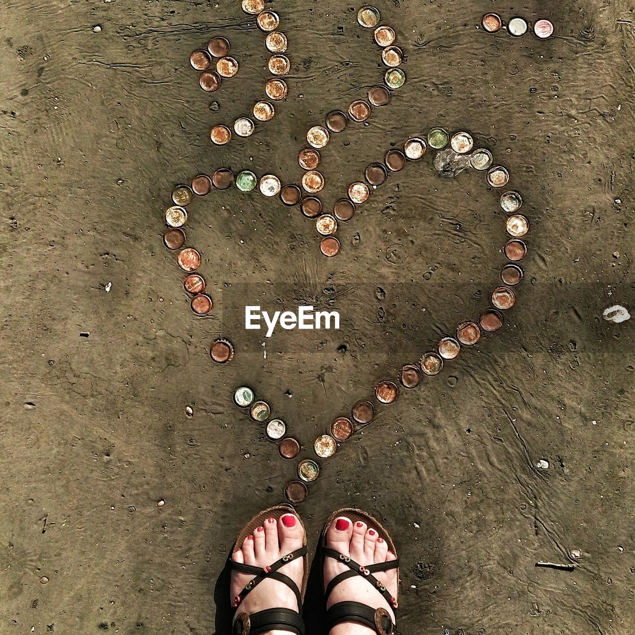 Directly above shot of womans feet near heart shape made with bottle caps