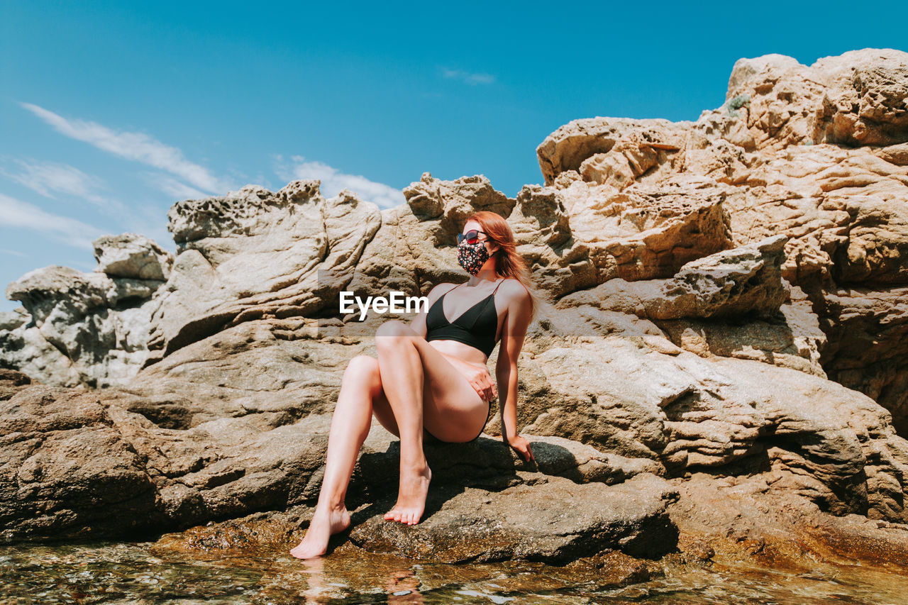 REAR VIEW OF WOMAN SITTING ON ROCK