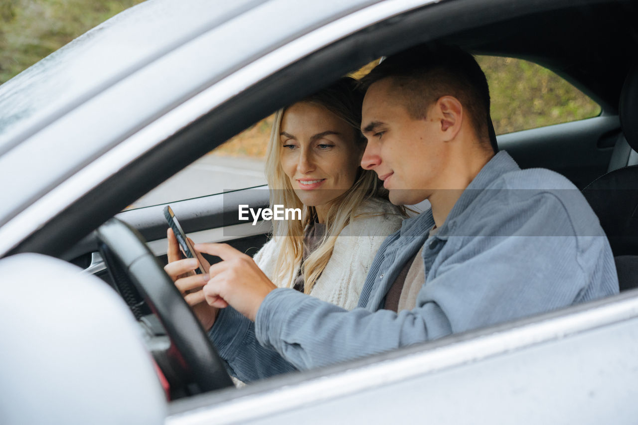 A young couple on a road trip looking at a map on their phone in a navigator.