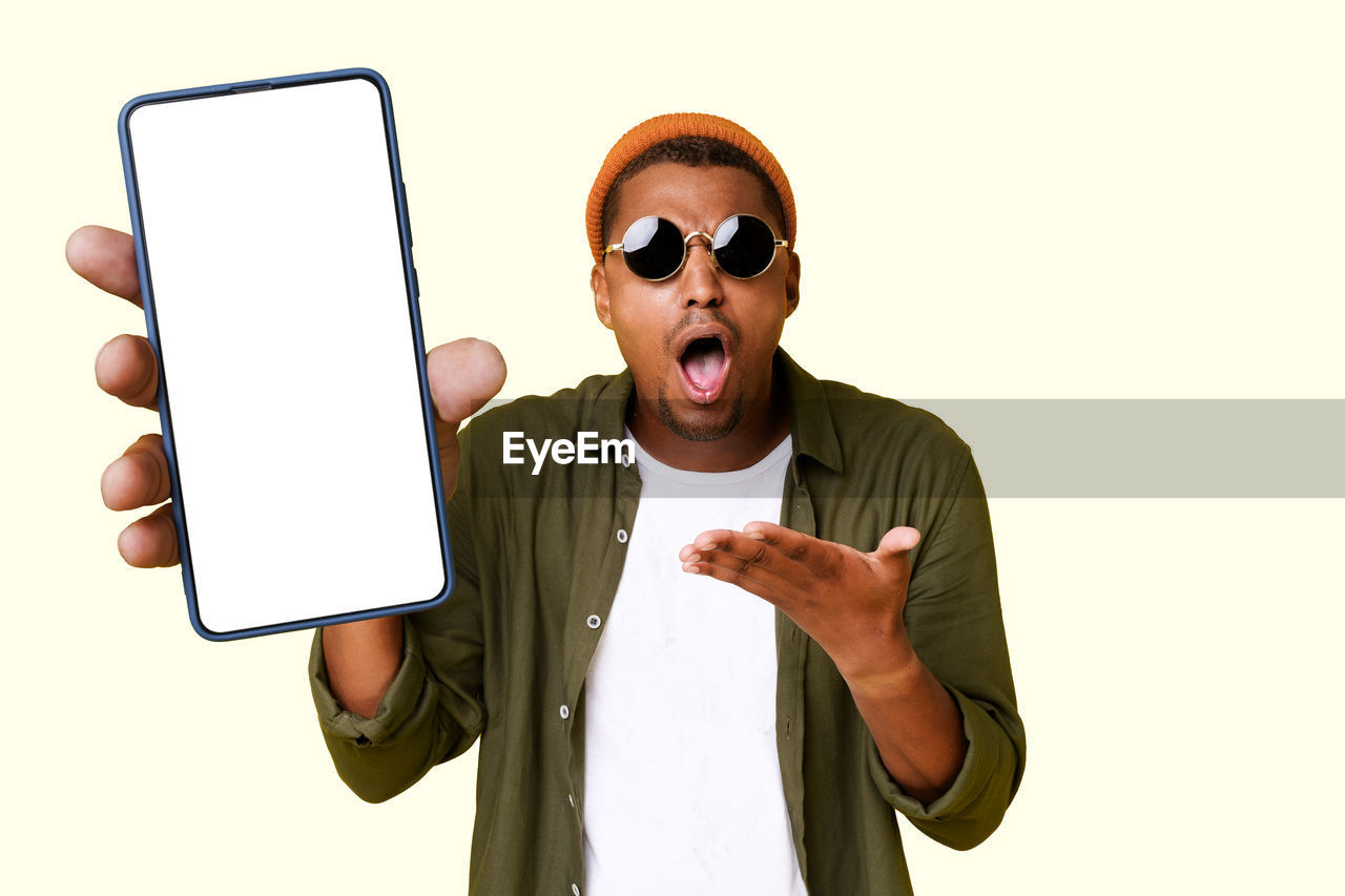 communication, technology, men, finger, adult, one person, fashion, wireless technology, person, gesturing, glasses, sunglasses, white background, cut out, studio shot, holding, clothing, emotion, fun, showing, hand, business, human mouth, copy space, humor, human face, shouting, mobile phone, facial expression, front view, smartphone, mouth open, waist up, indoors, portrait, computer, portable information device, arts culture and entertainment, businessman, pointing