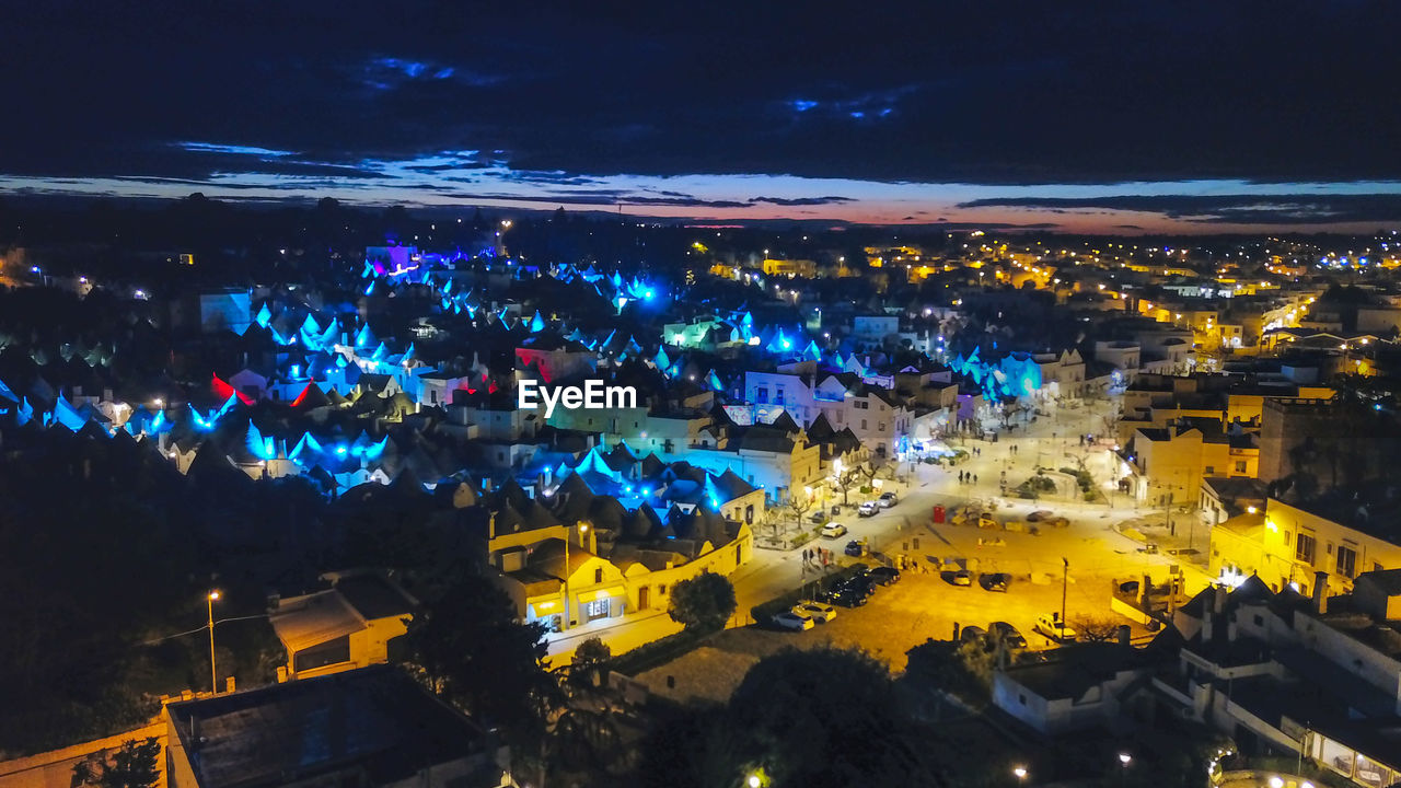 HIGH ANGLE VIEW OF ILLUMINATED STREET AMIDST BUILDINGS IN CITY
