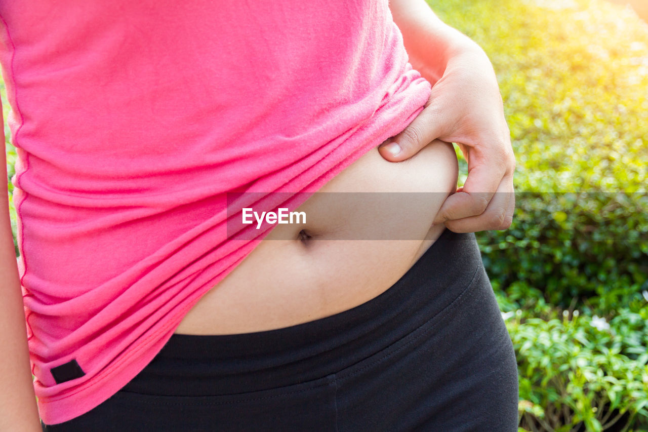 Midsection of woman pinching her belly outdoors