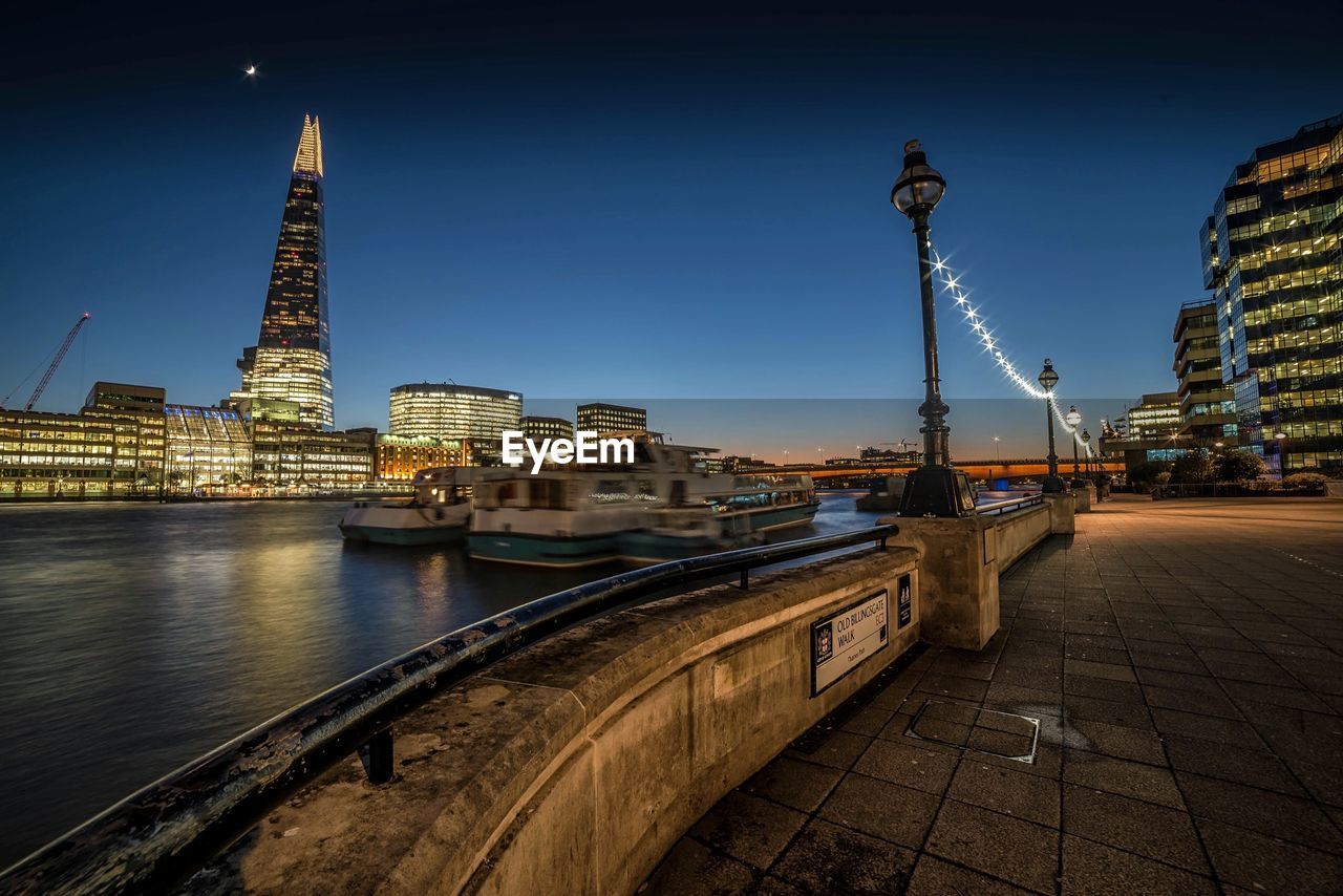 Illuminated shard london bridge by thames river against sky at night