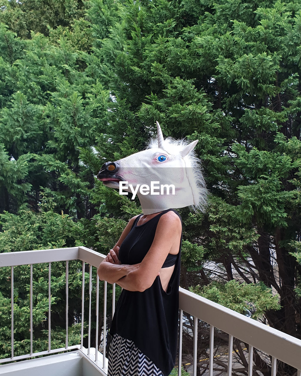 Woman wearing mask while standing by railing against trees